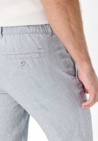 Light gray linen trousers featuring a back pocket with a button and a small logo. The fabric has a subtle texture and casual fit.