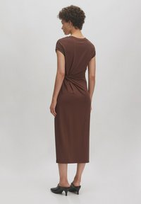 Braunes Midikleid mit lässigem Schnitt, kurzen Ärmeln, verdrehtem Rücken und glatter Textur. Tragen mit schwarzen Absatzmules.