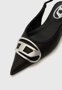 Toc cu slingback negru, cu vârful ascuțit, având un accent metalic argintiu în partea din față. Textură netedă cu un ușor luciu.