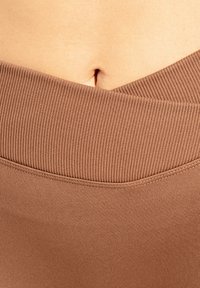 Brauner, gerippter Bund an einem Kleidungsstück, der eine glatte Stoffstruktur zeigt und oben eine leichte Kurve aufweist, die eine kleine Hautpartie freilegt.