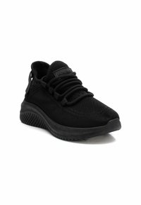 Zapato deportivo negro con parte superior de malla, superficie texturizada, suela flexible y sistema de cordones. Presenta un talón elevado y un detalle de logo característico.