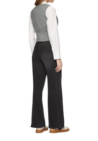 Grijs geknipt vest over een witte blouse met lange mouwen, gecombineerd met zwarte flared jeans en beige schoenen met bruine zolen.