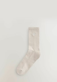Lysbeige knæstrømper med ribbet struktur og et lille broderet "self" logo på den øverste del af benet. Glat finish og rund tå.