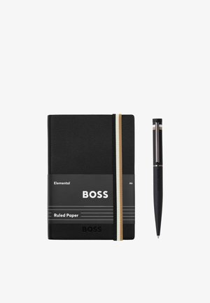 Carnet A6 à lignes noir avec élastique et stylo assorti, tous deux de la marque "BOSS", disposés côte à côte sur un fond blanc.