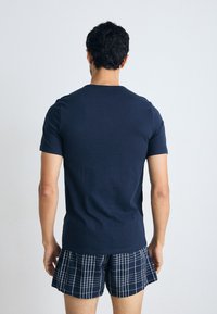 T-shirt de algodão azul-marinho com mangas curtas e decote redondo, combinado com calções xadrez em azul-marinho e branco. Tecido texturizado.