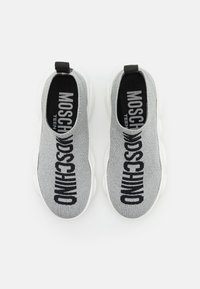 Graue Strick-Slipper mit einer weißen Sohle, auf der "MOSCHINO" in schwarzer Schrift über die Oberseite gedruckt ist. Texturiert, minimalistisch im Design.
