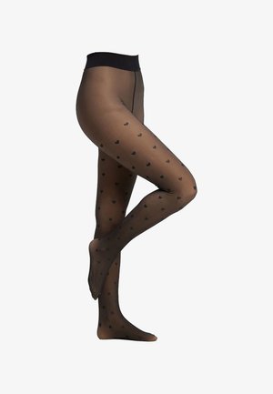 Benen in zwarte doorschijnende panty’s met kleine zwarte hartjespatronen, met één voet plat en de andere achter de knie opgetrokken.