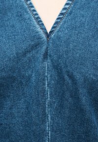 Κοντινή λήψη υφάσματος από μπλε τζιν με ραφή σε σχήμα V και λεπτομέρεια ραφής σε καφέ απόχρωση σε ένδυμα.