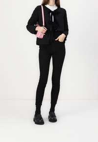Sort quilted jakke med en sløjfedetalje, parret med sorte skinny jeans og sorte loafers. En lille pink crossbody taske tilføjer farvekontrast.