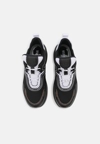 Černobílé tenisky s texturovaným síťovaným svrškem, polstrovaným límcem a kontrastními akcenty. Obsahují tkaničky a konstrukci gumové podrážky.