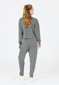 Grijze trainingsoutfit van zacht materiaal, met een relaxte pasvorm, drop shoulders, tapered broeken en ribbels aan de mouwen, gecombineerd met witte sneakers.