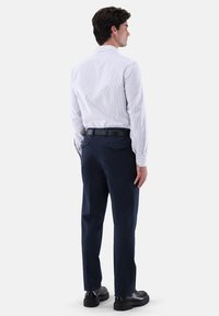 Weiß gestreiftes Langarmhemd mit Knopfmanschetten, kombiniert mit navyblauen Hosen. Beide Kleidungsstücke haben einen maßgeschneiderten Schnitt und standardmäßige Taschen.