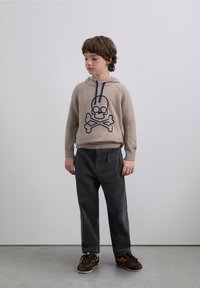 Beiger Hoodie mit einem dunkelblauen Totenkopf- und Knochen-Design, kombiniert mit dunkelgrauen Cordhosen und braunen Sneakers. Schlichter Hintergrund.