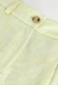 Tissu vert clair avec un motif jacquard floral subtil, comportant un bouton et une passoire de ceinture à la taille.