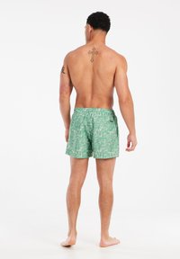 Gröna mönstrade badshorts med en mjuk textur, elastisk midja och en liten bakficka. Har en tropisk tryckdesign.
