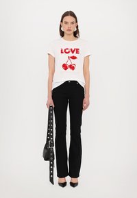 T-shirt bianca con testo rosso "LOVE" e grafica di ciliegia, abbinata a pantaloni neri a zampa d'elefante e una cintura borchiata. Scarpe nere a punta.
