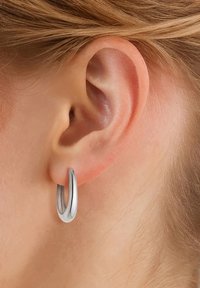 Boucle d'oreille en argent avec une finition polie, présentant un design arrondi et lisse qui pend du lobe de l'oreille.
