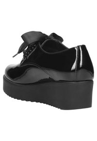 Scarpe con plateau in vernice nera, con punta arrotondata e un grande fiocco in raso sulla parte superiore. Suola testurizzata per una maggiore aderenza.