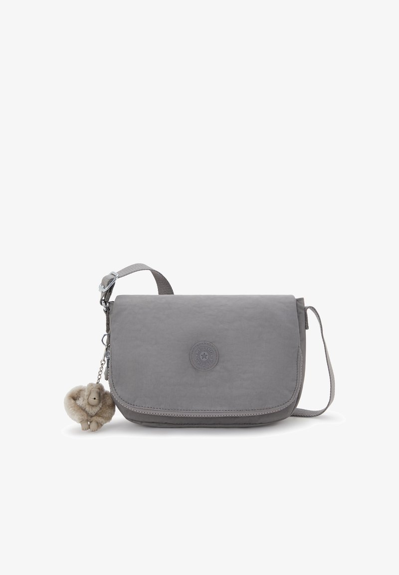 Graue Umhängetasche mit Klappenverschluss, verstellbarem Tragegurt, runder Logo-Applikation und angehängtem Plüschaffen-Schlüsselanhänger.