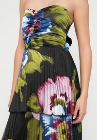 Robe sans manches à fleurs avec une jupe plissée noire, des motifs vibrants en bleu, vert et rose, et des détails froncés au niveau du bodice.