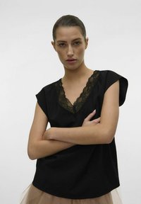 Top nero a maniche corte con scollo a V decorato da un intricato bordo in pizzo nero. Tessuto soffice con vestibilità rilassata e leggero drappeggio.