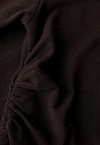 Nahaufnahme von dunkelbraunem geripptem Stoff mit gerafftem Rüschendetail, das strukturierte Falten bildet.