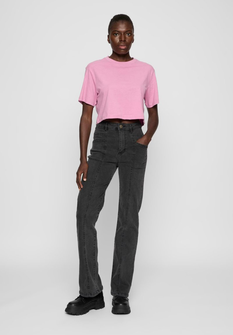 Rosa, kort T-skjorte med kort erme, kombinert med høyt liv sorte jeans. Jeansene har frontlommer og rett ben-design. Sorte ankelstøvler.