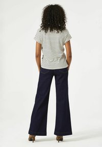 Top de manga corta a rayas en crema y negro, combinado con pantalones de mezclilla de pierna ancha en azul oscuro. Costuras de contraste notables en los pantalones.