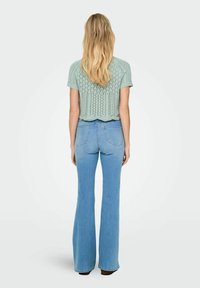 Lysgrøn strikket crop top med korte ærmer, parret med blå flagrende jeans. Toppen har en bølget kant og hulmønster.