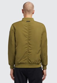 Olive rohelise värvi bomber-jakk, kerge kangas, soonikkoes krae ja varrukad, sile tekstuur, keskelt alla vertikaalne õmblus, nähtavad logod puuduvad.