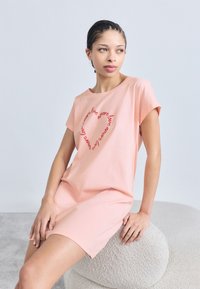 Ροζ φόρεμα με κοντά μανίκια και άνετη εφαρμογή, με σχέδιο κειμένου σε σχήμα καρδιάς σε κόκκινο χρώμα. Μαλακό βαμβακερό υλικό και λεία υφή.