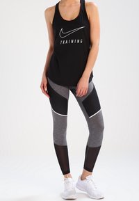 Czarny podkoszulek Nike z napisem "TRAINING", w zestawie z legginsami w szaro-czarne wzory z siateczkowymi akcentami. Białe buty sportowe.