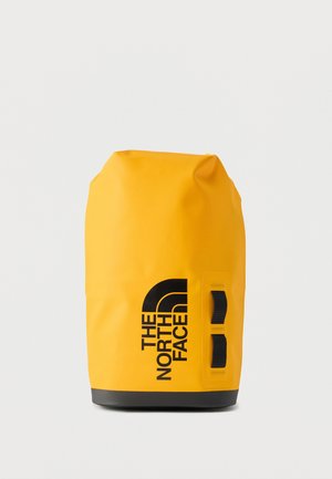 Gele waterdichte droogtas met zwarte onderkant, zwart logo "The North Face" en twee zwarte zijhandvatten op een effen achtergrond.