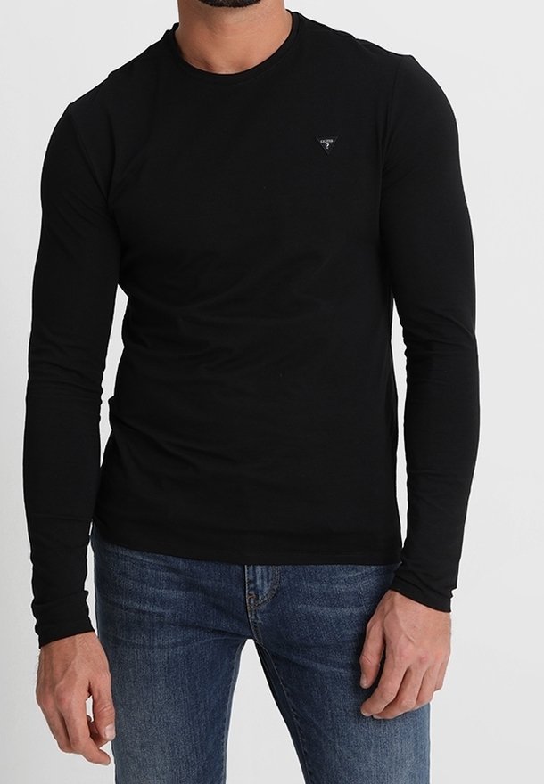 T-shirt noir à manches longues en matériau doux, avec un col rond et un petit logo sur la poitrine. Associé à un jean bleu.