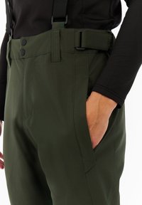 Groene waterdichte broek met een hoge taille, verstelbare bretels, twee zijzakken en een gladde textuur. Vastgemaakt met knopen en een riem.