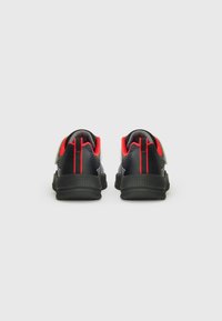 Chaussures de sport noires et rouges avec une surface texturée, comportant un dessus en maille, un col rembourré et des accents réfléchissants à l'arrière.