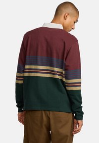 Camisa de manga larga con un diseño a rayas en color burdeos, marino y verde, que presenta un collar blanco, tejido texturizado y un corte relajado.