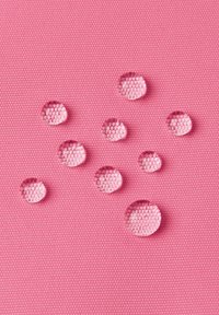 Gocce d'acqua trasparenti riposano su una superficie testurizzata di colore rosa, presentando una forma rotonda e dimensioni varie, che migliorano l'aspetto tattile della superficie.