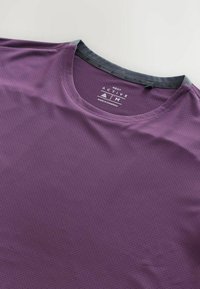 Paars geperforeerd actief T-shirt met een zwarte ribgebreide Hals. Heeft "NEXT ACTIVE" branding in de nekzone. Gemaakt in Cambodja.