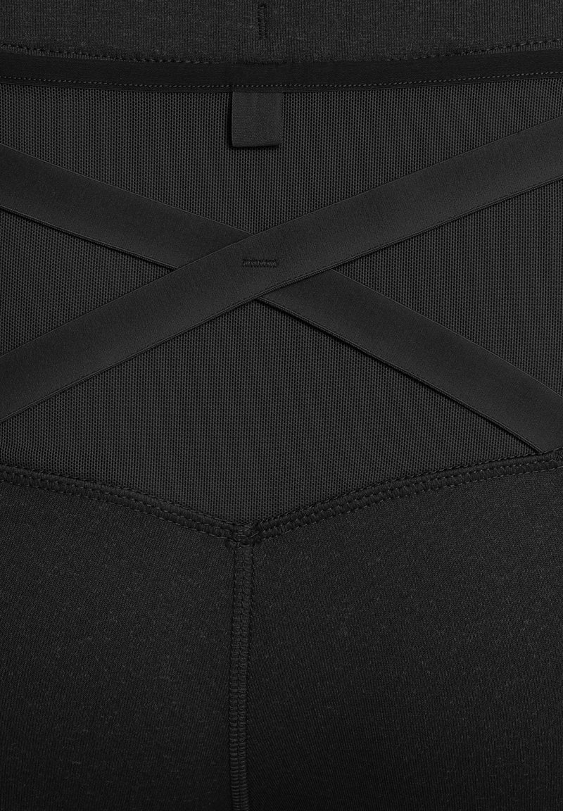 Leggings de deporte negros con un panel de malla texturizada y un diseño de tiras entrelazadas en la parte posterior. Presenta costuras planas y un acabado suave.