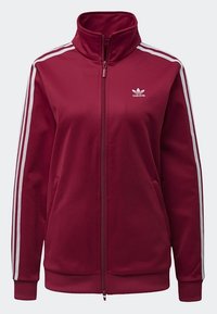 Bordeauxroter Reißverschlussjacke mit hohem Kragen, weißen Streifen an den Ärmeln, kleinem weißen Logo auf der Brust, weichem Material und seitlichen Taschen.