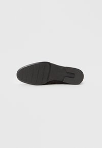 Suela de zapato negro tipo slip-on con goma texturizada, que presenta un patrón estriado para mayor agarre y un acabado liso en los bordes. Sin logotipos ni marcas visibles.