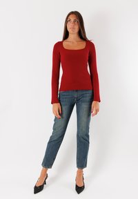 Top lungo a maniche ribattute rosso con scollatura quadrata, abbinato a jeans dritti azzurri chiari e décolleté nere a punta.