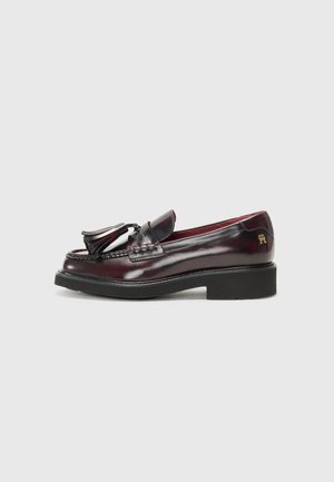Burgunderrøde læderloafers med frynser, sort sål, lav hæl og gyldent logodetalje på hælen, vist i sideprofil på hvid baggrund.