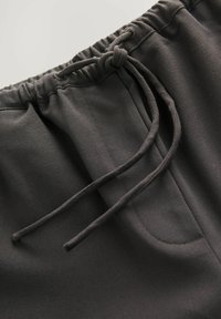 Sorte sweatpants med snøre i taljen, tætsiddende ben og glat tekstur med sidelommer. Enkel design til afslappet brug.