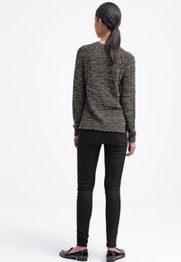 Svart texturerad tröja med långa ärmar, rund halsringning och en avslappnad passform, ihop med smala svarta jeans och platta skor.