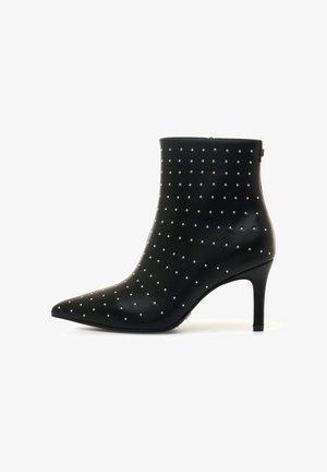 Stivale alla caviglia in pelle nera con punta affusolata, caratterizzato da borchie argentate disposte in un motivo. Il tacco a stiletto misura circa sette centimetri.