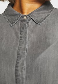 Grijze denim overhemd met een spitse kraag, een voorzijde knoopsluiting en een zachte textuur. Zichtbare stiksels langs de randen en de knoopsluiting.