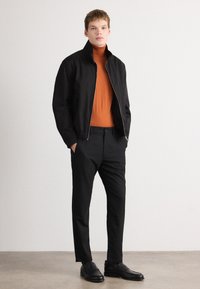 Pánska čierna ľahká bunda so zipsom, oranžový rolák a čierne elegantné nohavice. Hladká tkanina a štýlový dizajn.