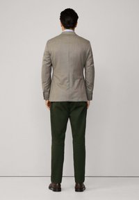 Ljust grå passform blazer med slag, matchad med mörkgröna byxor. Läder skor fulländar outfiten, sedd bakifrån.